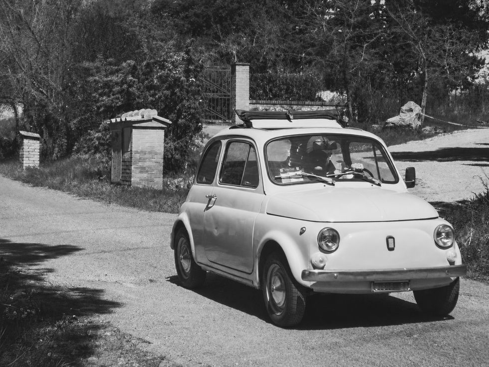 Black and white photograph of a vintage Fiat on a quiet rural road