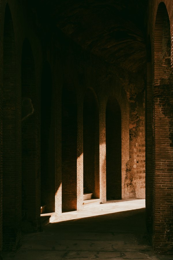 Dim brick arcade with repeating arches and warm light falling across the floor